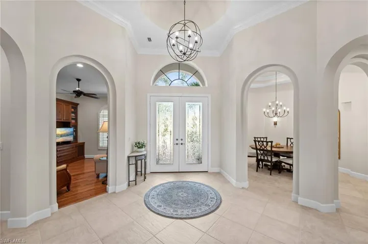 Grand foyer entry featuring arched doorways, light-toned tile flooring, double doors with decorative glass, a transom window, and a spherical chandelier