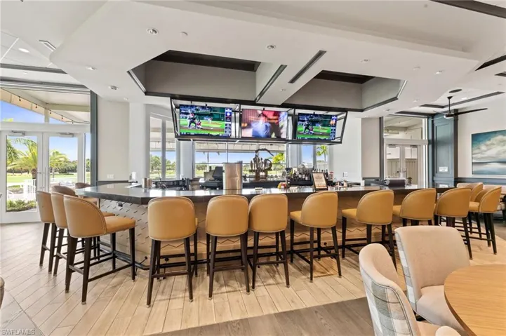 Spacious bar area with wood-finish flooring, a long bar with stone countertop, and built-in display screens