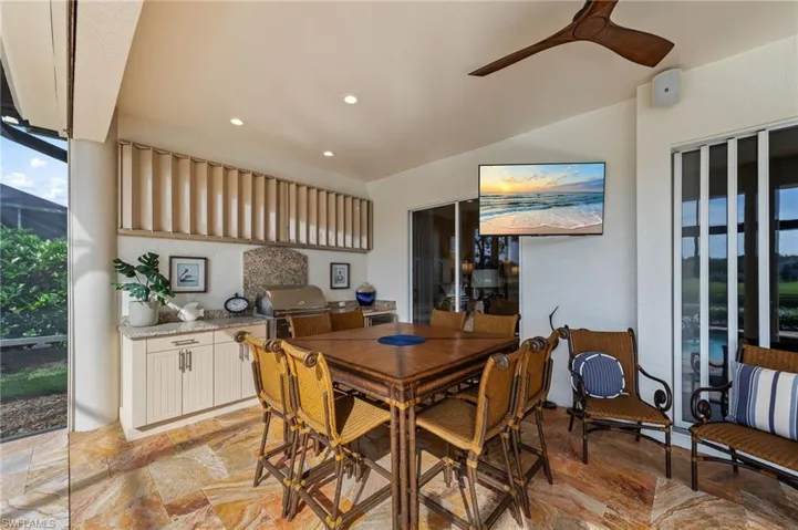 Expansive screened lanai featuring an outdoor kitchen with integrated grill, stone countertops, and cabinetry
