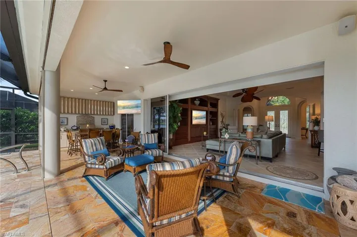 Spacious covered patio featuring stone-finish flooring, ceiling fans, and an outdoor kitchen with built-in cabinetry