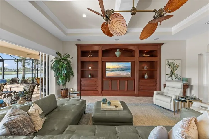 Living area with coffered ceiling and dual ceiling fans, featuring a built-in wood-finish entertainment center with integrated shelving and cabinetry