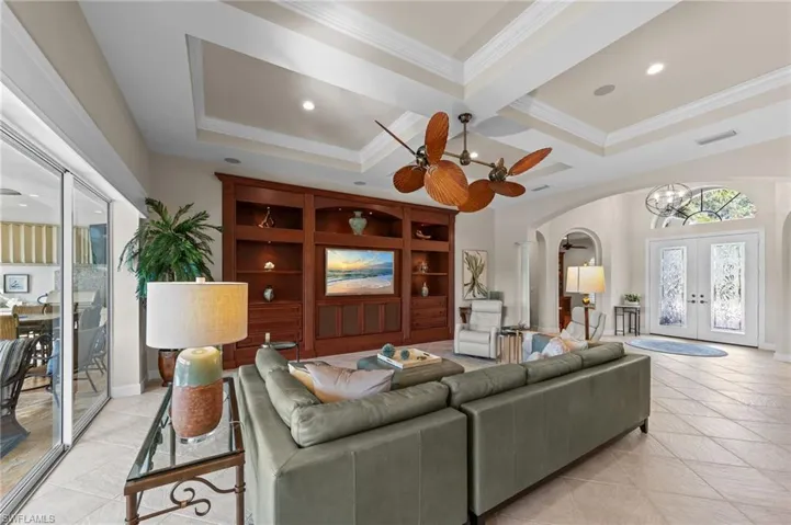 Expansive living area featuring a built-in wood entertainment center, coffered ceilings with recessed lighting, and large format tile flooring