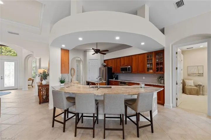 Open-concept kitchen featuring an expansive island with seating, warm wood cabinetry, stainless steel appliances, and a tiled backsplash