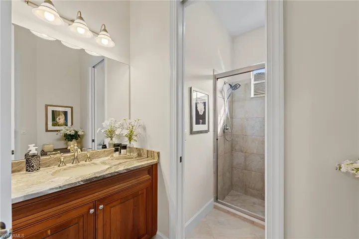 Bathroom featuring a rich wood-tone vanity with a light-toned countertop, dual undermount sinks with polished hardware, a large wall mirror, and a glass-enclosed shower with tiled walls and flooring