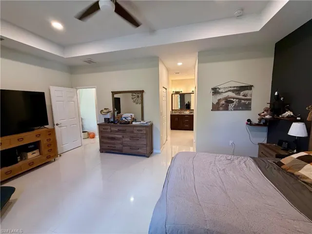 Bedroom featuring a ceiling fan, a tray ceiling, ensuite bathroom, and recessed lighting