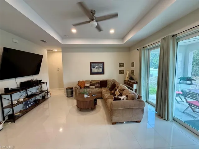 Living room featuring a ceiling fan, a tray ceiling, light tile patterned floors, and recessed lighting