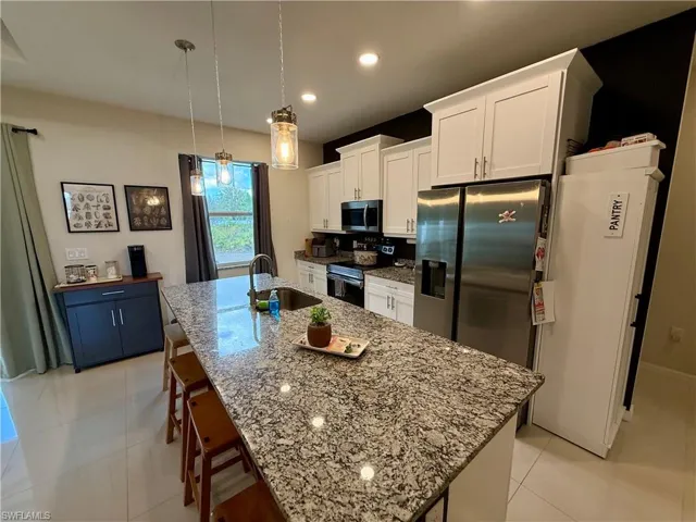 Kitchen with a kitchen bar, stainless steel appliances, a center island with sink, light stone counters, and white cabinets