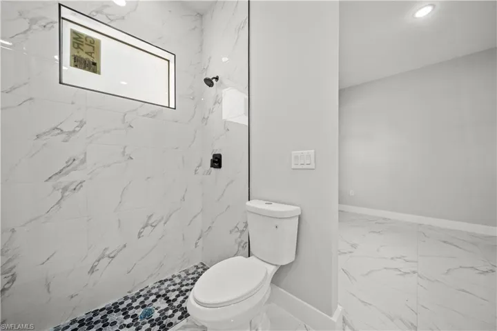 Full bath with marble finish floor, toilet, baseboards, and a tile shower