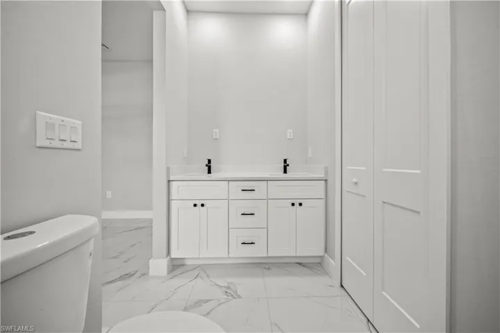 Full bathroom featuring toilet, a sink, marble finish floor, baseboards, and double vanity