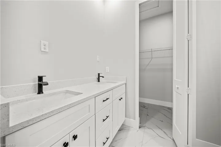 Bathroom with a spacious closet, marble finish floor, a sink, and baseboards