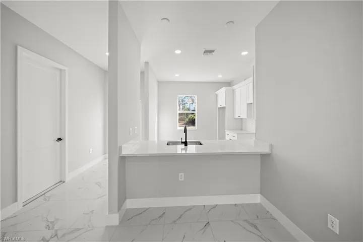 Kitchen featuring white cabinetry, light countertops, recessed lighting, baseboards, and a sink
