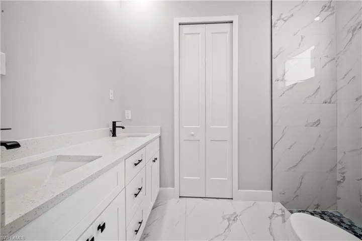 Bathroom with marble finish floor, a sink, double vanity, and baseboards