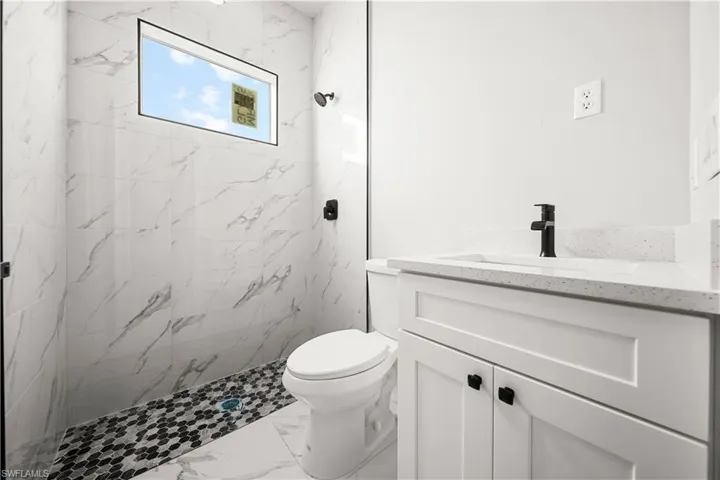Bathroom featuring marble finish floor, a marble finish shower, toilet, and vanity