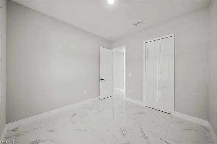 Unfurnished bedroom featuring baseboards, marble finish floor, visible vents, and a closet