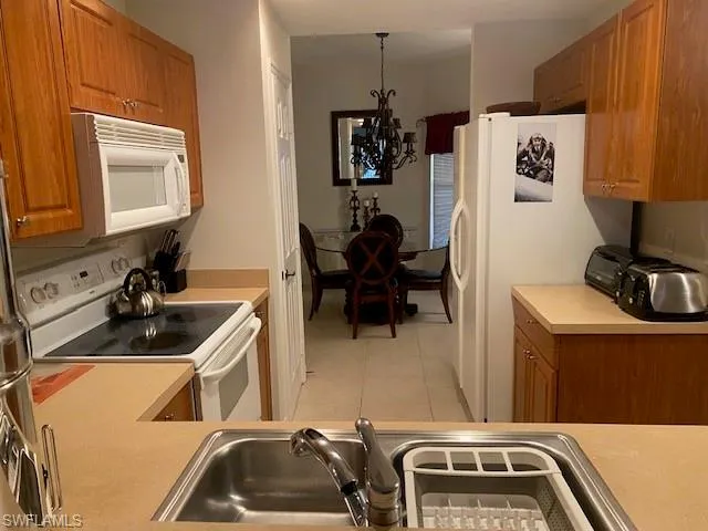Kitchen with hanging light fixtures, sink, light tile patterned flooring, a notable chandelier, and white appliances