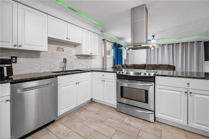 White shaker cabinetry, dark countertops, stainless steel appliances, tile backsplash, and wood-finish flooring