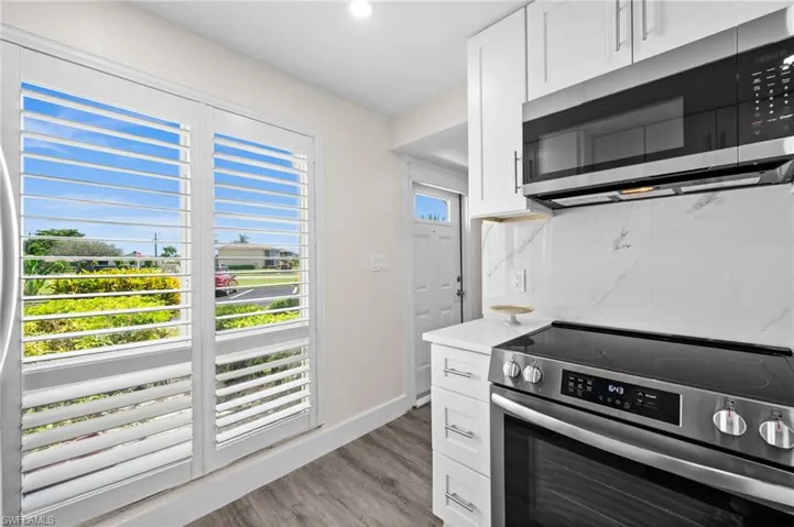 Kitchen with stainless steel appliances, white cabinetry, light wood-style flooring, and light stone countertops