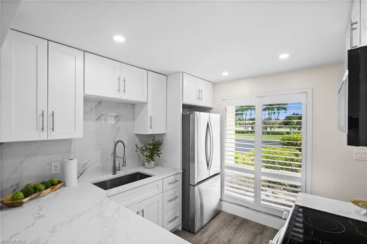 Kitchen with white cabinets, black appliances, light stone counters, decorative backsplash, and recessed lighting