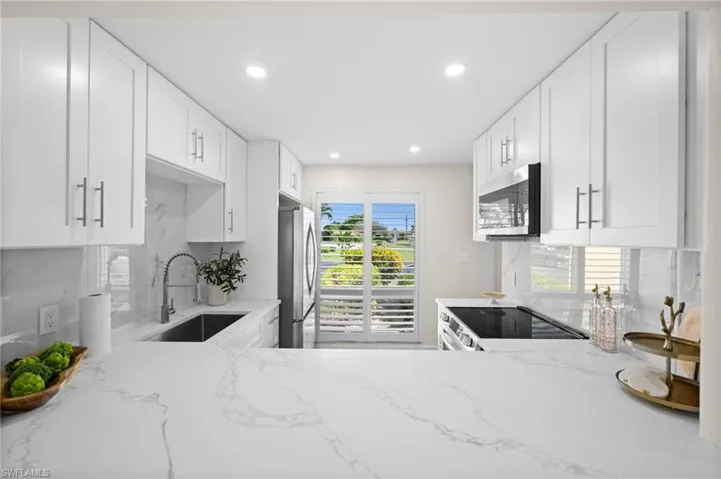 Kitchen with white cabinets, light stone counters, backsplash, appliances with stainless steel finishes, and recessed lighting