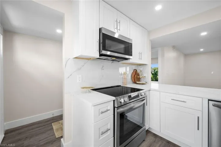 Kitchen with stainless steel appliances, recessed lighting, white cabinetry, light stone counters, and dark wood-type flooring
