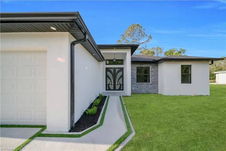 Doorway to property with stucco siding, a garage, a lawn, and stone siding