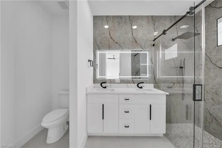 Bathroom with a sink, double vanity, a marble finish shower, and toilet