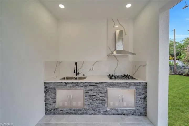 Kitchen featuring gas cooktop, wall chimney exhaust hood, a sink, backsplash, and light tile patterned floors