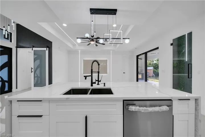 Kitchen with a tray ceiling, a notable chandelier, a sink, white cabinetry, and dishwasher