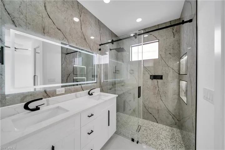 Bathroom with double vanity, tile walls, a sink, and a marble finish shower