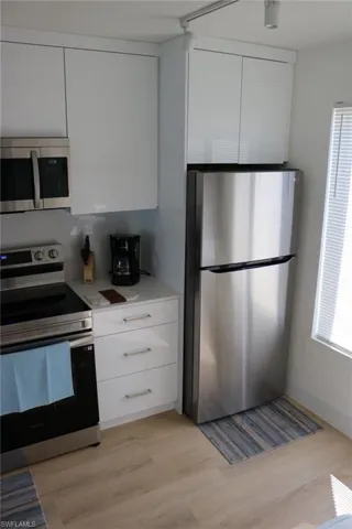 Compact kitchen featuring stainless steel appliances, white cabinetry, track lighting, light wood-finish flooring, and white countertops