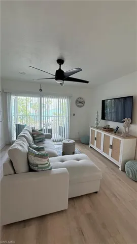 Bright living space featuring wood-finish flooring, a contemporary ceiling fan, and sliding glass doors with vertical blinds