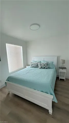 Spacious room featuring wood-finish flooring, a window with horizontal blinds, and a flush-mount ceiling light