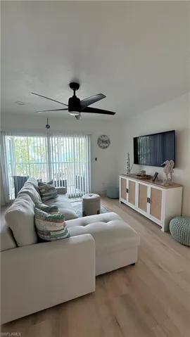 Living area featuring wood-finish flooring, a contemporary ceiling fan, and sliding glass doors with vertical blinds
