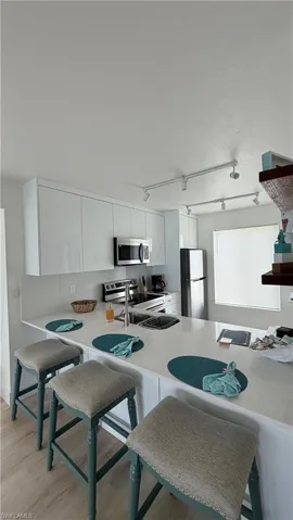 Kitchen featuring a large central island with seating, white cabinetry, stainless steel appliances, and track lighting