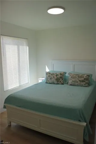Bedroom featuring light-tone wood-finish flooring, a window with blinds, and a ceiling-mounted light fixture