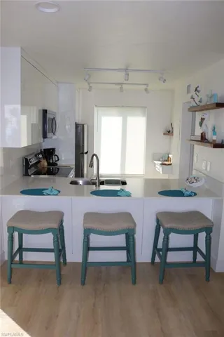 Kitchen featuring a peninsula with seating, a stainless steel sink with a high-arc faucet, and light-toned wood-finish flooring