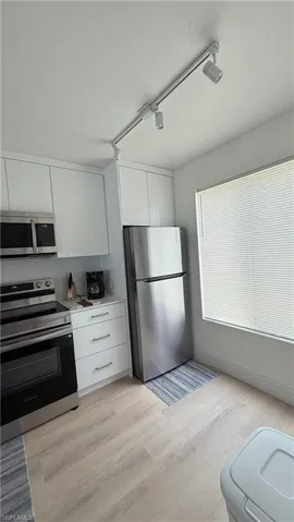 Kitchen featuring white cabinetry, stainless steel appliances, track lighting, and wood-finish flooring