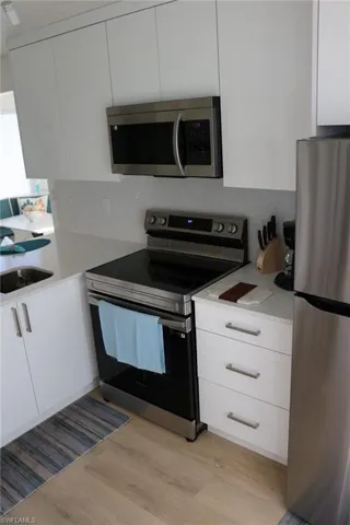 Modern kitchen featuring white cabinetry, stainless steel appliances, light wood-finish flooring, and white countertops