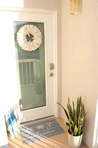 White entry door with integrated privacy blinds, complemented by a textured exterior wall and an outdoor wall-mounted light fixture
