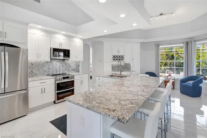 Kitchen with appliances with stainless steel finishes, backsplash, recessed lighting, white cabinets, and a kitchen bar