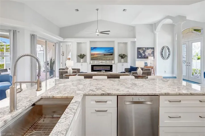 Kitchen featuring lofted ceiling, ceiling fan, decorative columns, white cabinetry, and open floor plan