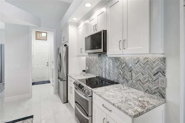Kitchen featuring stainless steel appliances, white cabinets, light stone countertops, and recessed lighting