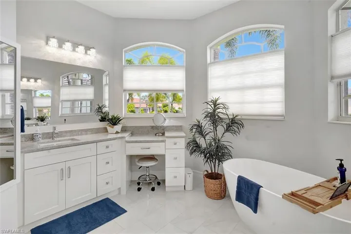 Bathroom with a freestanding tub, vanity, and marble look tile flooring