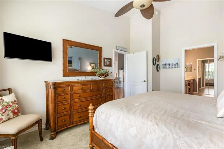 Primary Bedroom with high vaulted ceiling, light colored carpet, ensuite bath, and ceiling fan