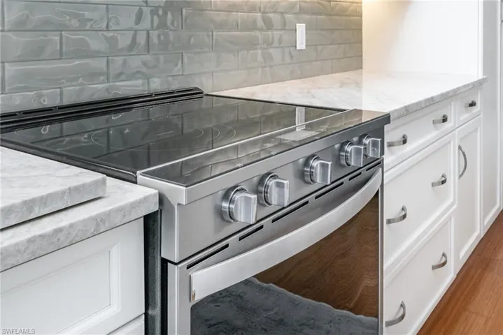 Kitchen view of high end smart stainless steel electric stove, decorative backsplash, light stone counters, and white cabinets