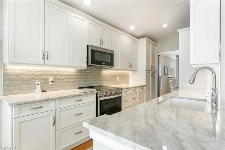 Kitchen with appliances with stainless steel finishes, a sink, light stone counters, white cabinetry, and recessed lighting
