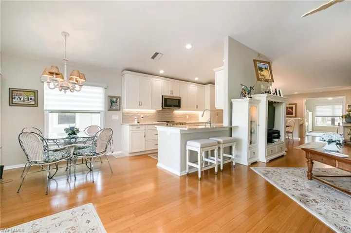 Kitchen featuring stainless steel microwave, a breakfast bar, a chandelier, decorative backsplash, and white cabinets