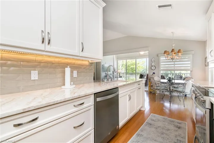 Kitchen with appliances with stainless steel finishes, a sink, vaulted ceiling, a chandelier, and white cabinetry