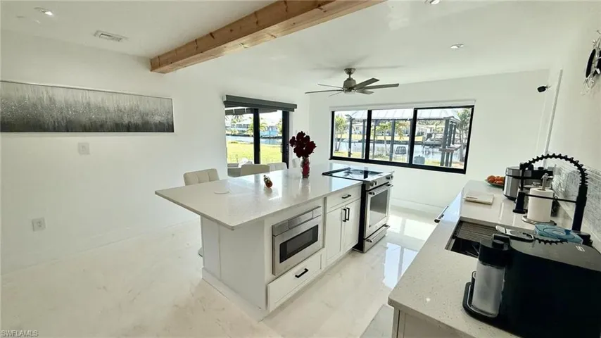 Kitchen with white cabinets, light stone countertops, stainless steel appliances, a kitchen island with sink, and beamed ceiling