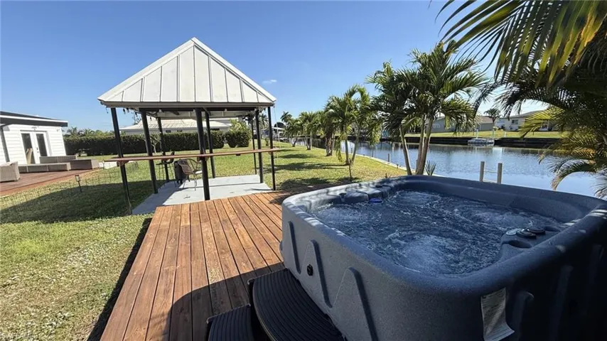 Dock area with a deck with water view, a hot tub, a gazebo, and a yard